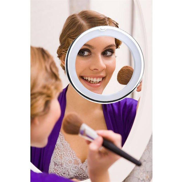 A woman smiles as she applies makeup using the UNIQ PRO BEAUTY Bathroom Mirror with LED Light and Suction Cup x10 Magnifying Mirror in white, mounted on her larger bathroom mirror.