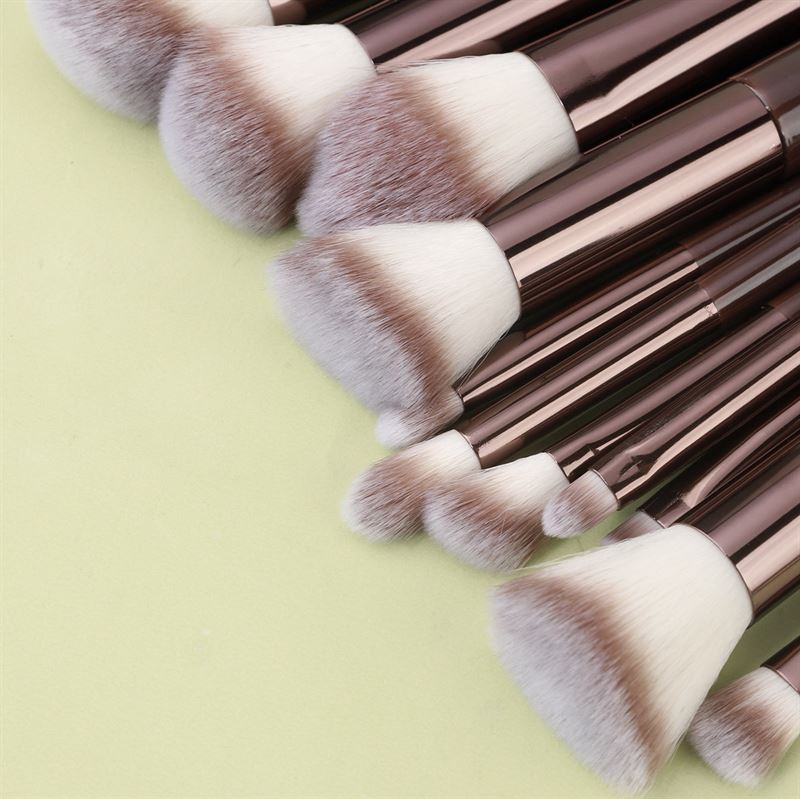 The Technique PRO Chocolate Bronze Makeup Brush Set (11 pieces) features brown handles and soft white bristles, stylishly displayed on a light green surface.