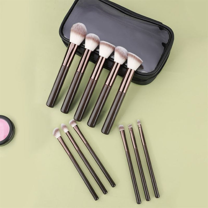 The Technique PRO Chocolate Bronze Makeup Brush Set (11 pieces) by Technique PRO, featuring dark handles and soft bristles, is displayed next to a black zippered case on a light green surface. A round pink powder container sits in the corner.
