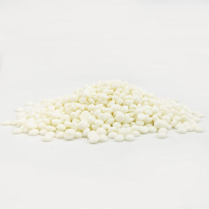 A pile of small, round, white UNIQ Nose Wax Kit pellets for nose hair removal by UNIQ is scattered on a plain white surface with a white background.